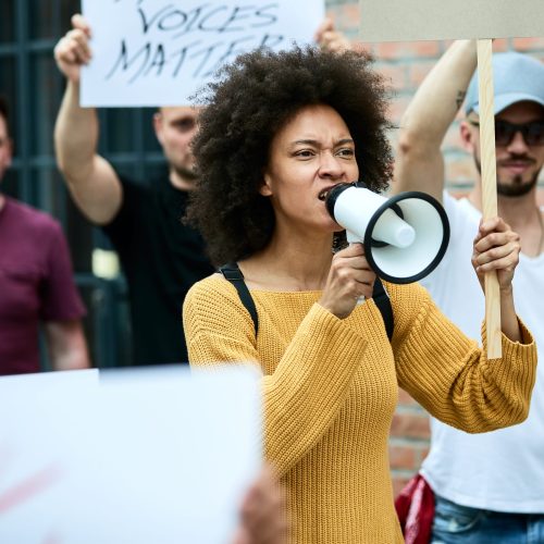 Displeased black woman participating in anti racism demonstrations and shouting through megaphone.